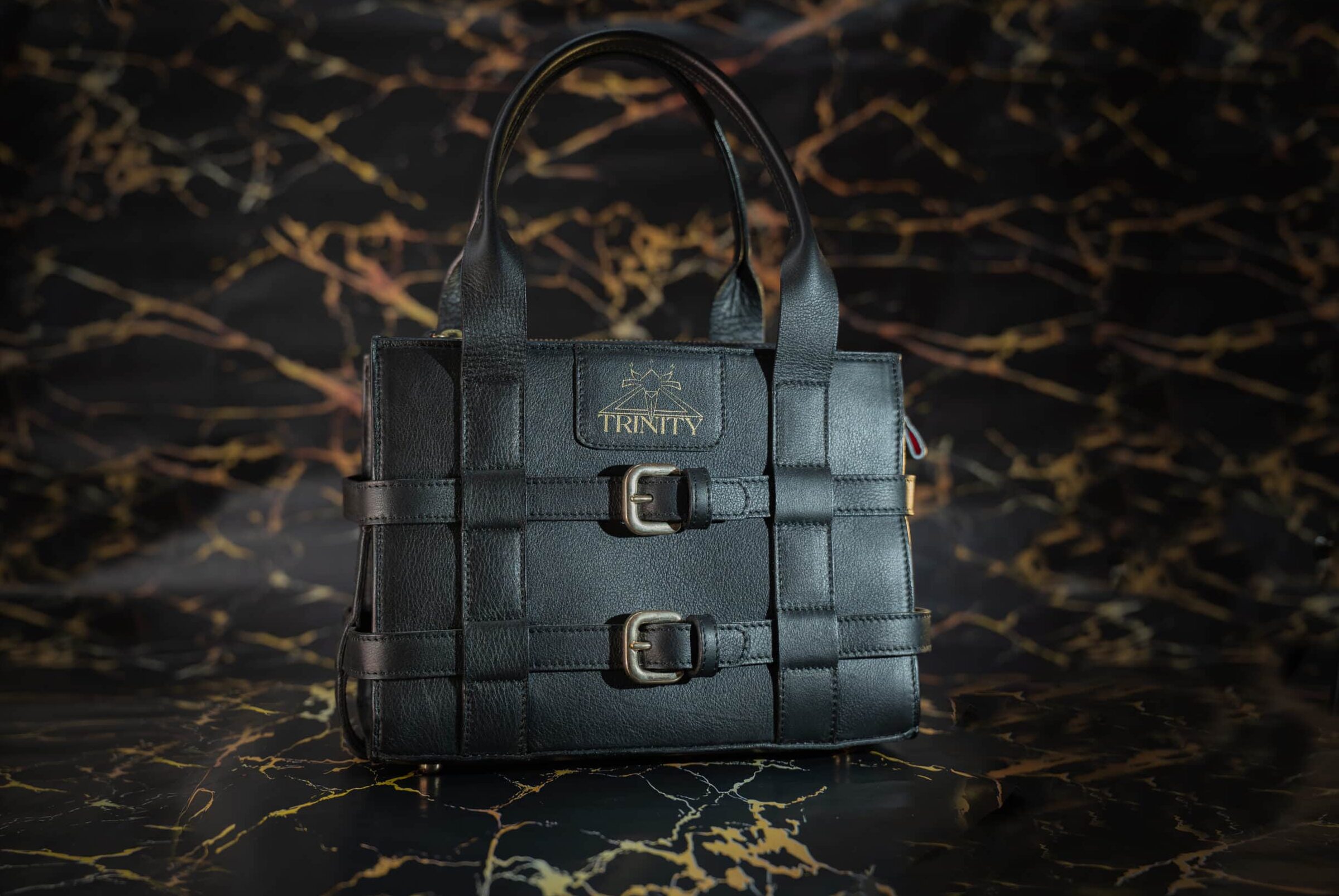 Bolso de mano de cuero vacuno negro con arnés envolvente y bandolera, interior de cuero de cordero rojo. Vista frontal.