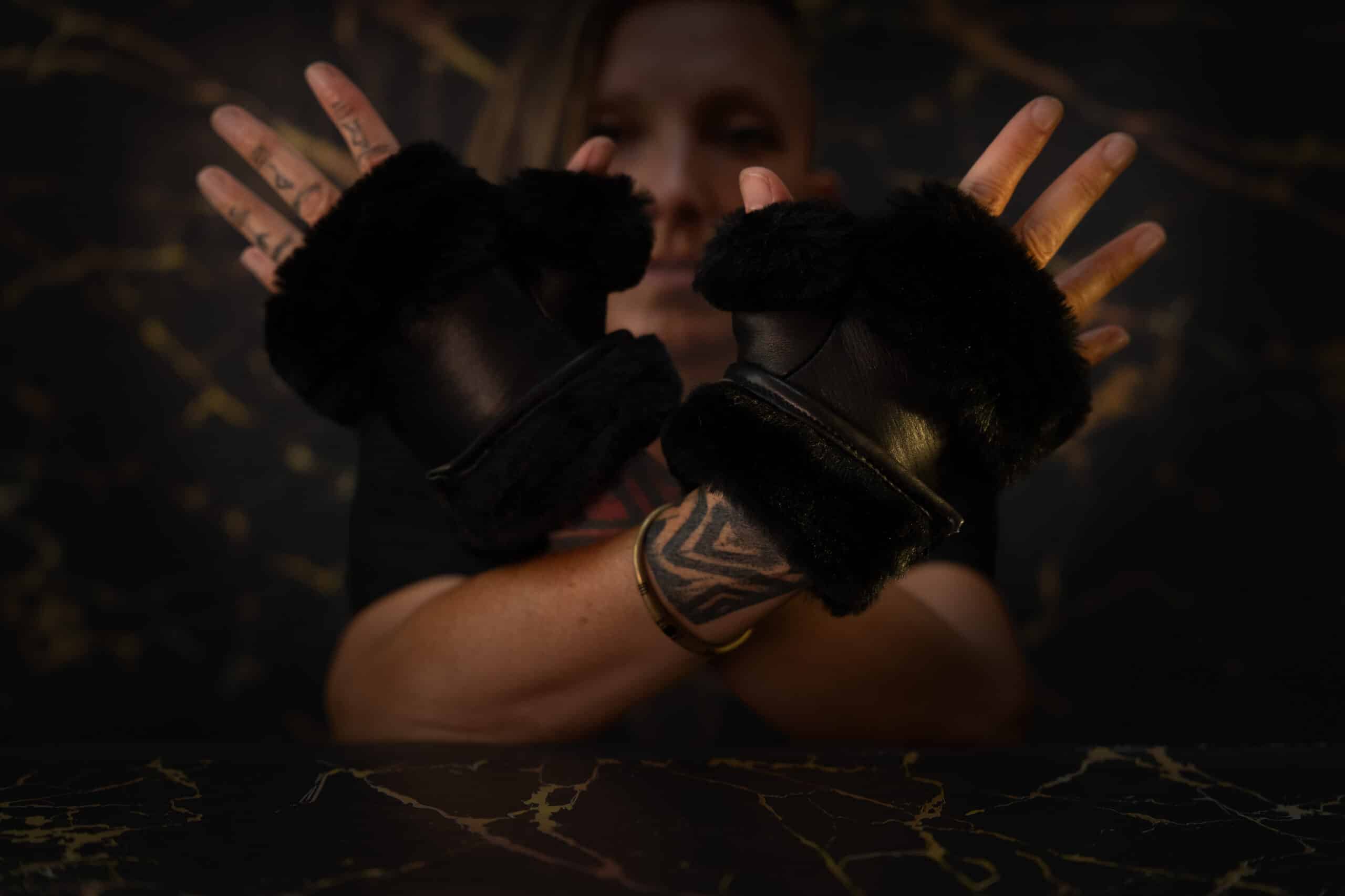 Guante mitón de cuero de cordero negro con pelo sintético negro, colocado en las manos de la modelo.